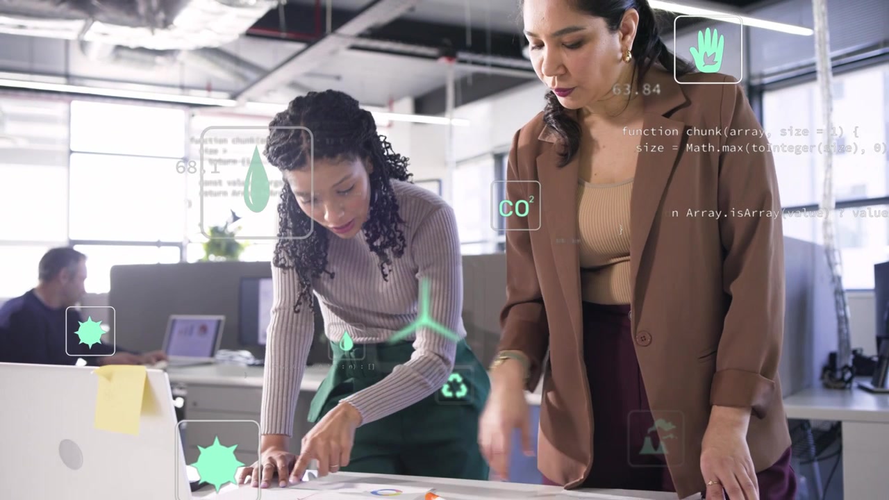 Uma segunda mulher se aproxima, a dupla organiza gráficos verdes e um laptop, revisando dados de CO2 exibidos por ícones de Realidade Aumentada.