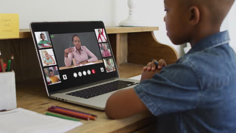 african american boy holding a pencil having a video conference on laptop at home