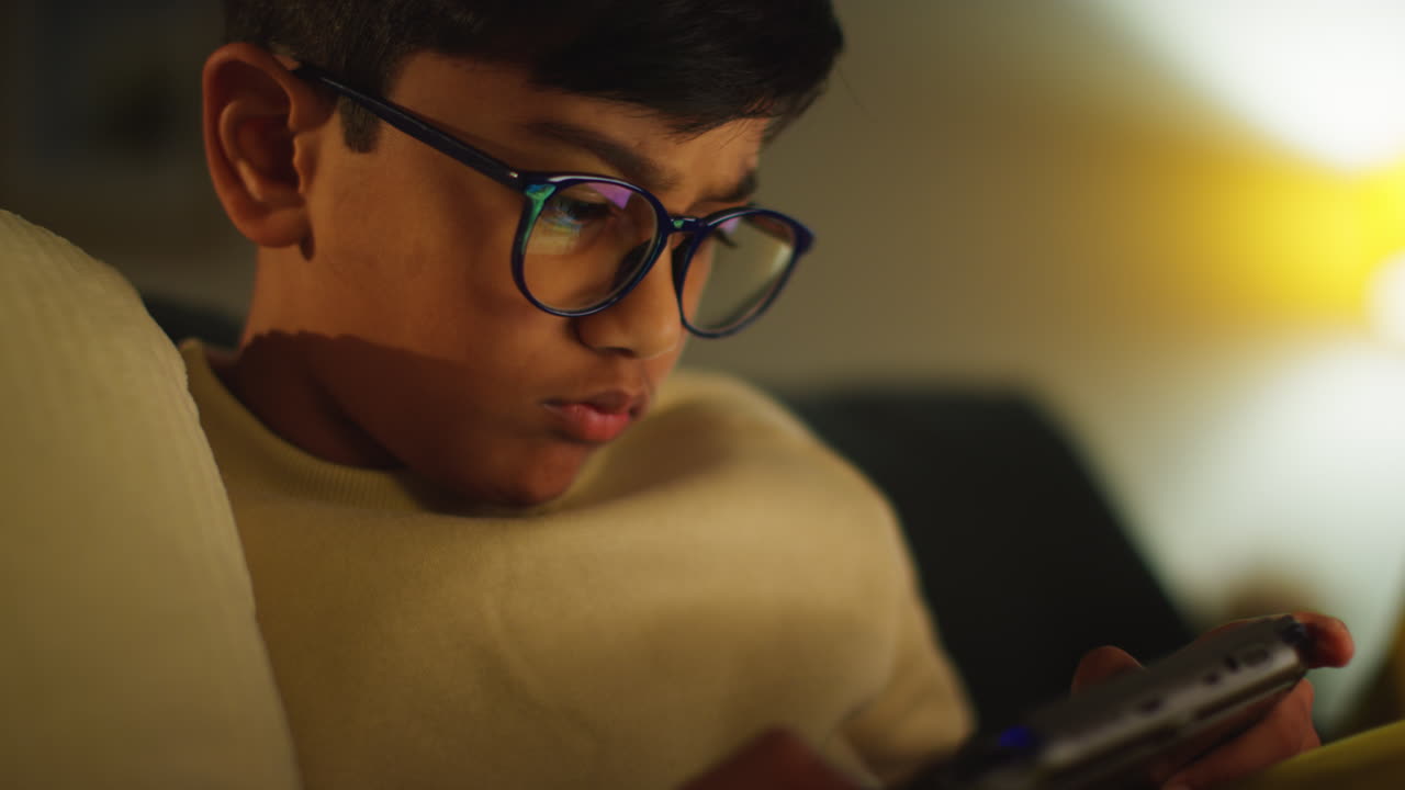 집에서 소파에 앉아서 게임을 하거나 밤에 휴대용 게임 장치에 스트리밍하는 어린 소년의 근접 사진