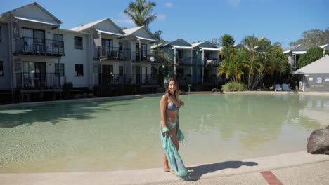 Modelo-Femenina-Sonríe-A-La-Cámara-Y-Da-La-Vuelta-En-El-Borde-De-La-Piscina-Del-Complejo-De-Lagos-Noosa