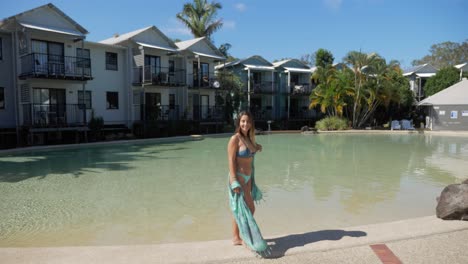 modelo femenina sonríe a la cámara y da la vuelta en el borde de la piscina del complejo de lagos noosa