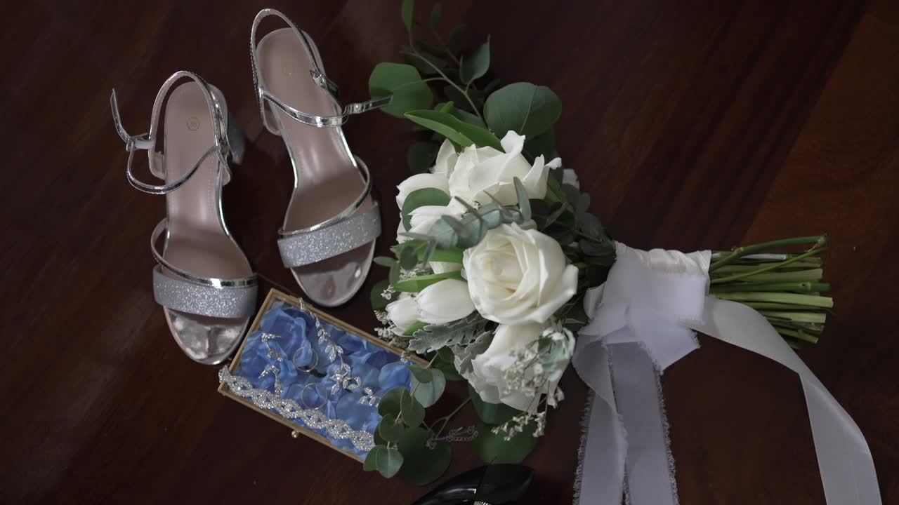 bridal arrangement featuring silver shoes, a white rose bouquet, and a delicate blue garter