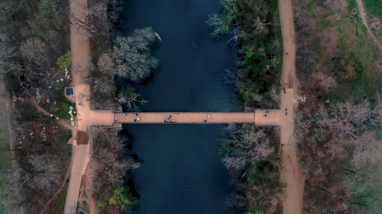 vista aérea de drones de personas y ciclistas cruzando un puente peatonal sobre el agua en un sendero en austin, texas