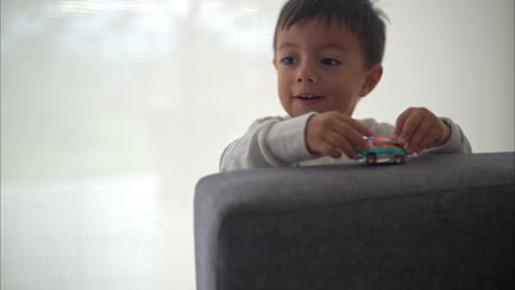 close up of a young hispanic boy playing with a blue car toy on a grey couch wearing pajamas on a cozy morning