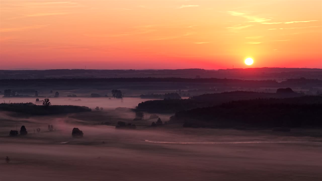 Drone view of foggy Polish fields at sunrise, warm orange glow, serene scene