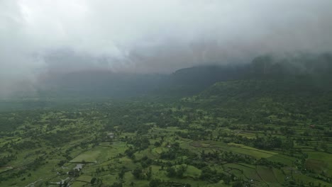 a stunning drone view of bhandardara, maharashtra, india, reveals lush green fields, misty mountains, and monsoon fog weaving through the landscape 4k