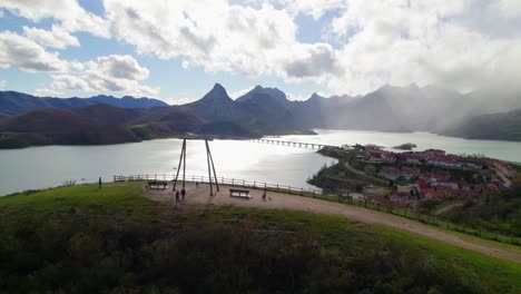 Parents-swinging-their-child-on-the-swing-at-the-viewpoint-in-Riaño,-a-village-in-León,-Spain-on-the-shore-of-a-large-reservoir-in-the-Cantabrian-mountains