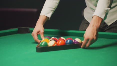 close-up of person's hands in white shirt carefully rolling a well-arranged set of colorful billiard balls in a triangle formation on green pool table. smooth movement and precise alignment