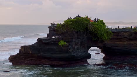 ancient balinese temple pura batu bolong on natural arch bridge in the sea in tanah lot, bali island, indonesia