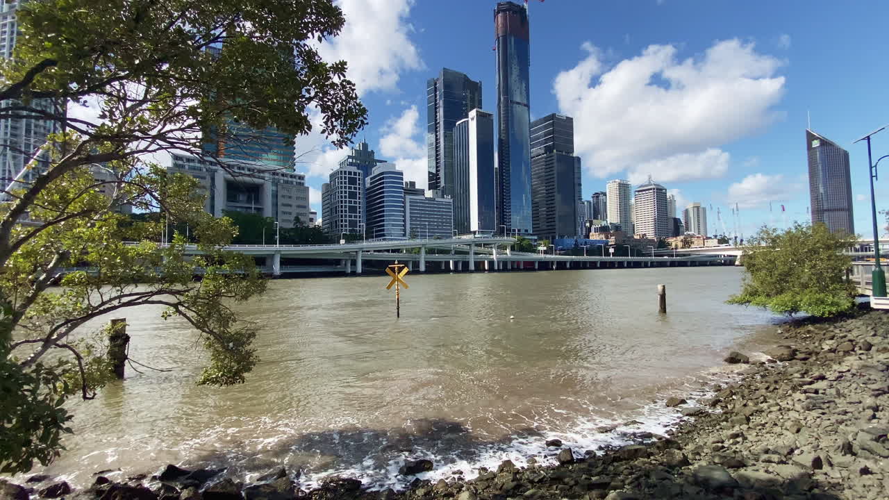 Waves break on the rocks of the Brisbane River with City buildings in the background, Queensland, Australia