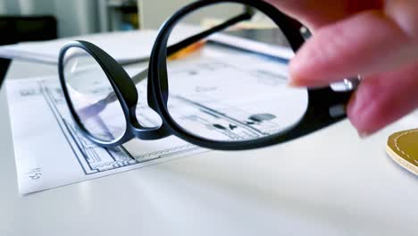 An-architect-picks-up-her-glasses-while-reviewing-blueprints---isolated-on-glasses-and-desk-workspace