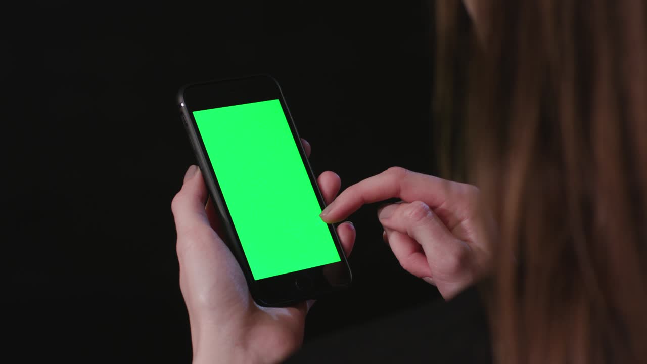여성은 초록색 스크린 스크롤로 전화를 들고 있습니다.