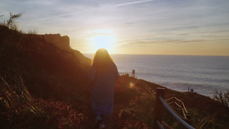 mujer caminando a lo largo del acantilado costero al atardecer
