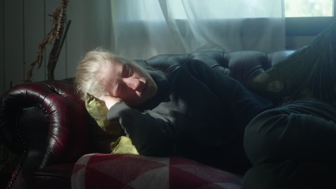 소파에서 자고 있는 아름다운 금발 소녀의 클로즈업, 거실의 소파에서 잠을 자고 있는 여성, 그녀의 얼굴에 춤추는 빛 광선