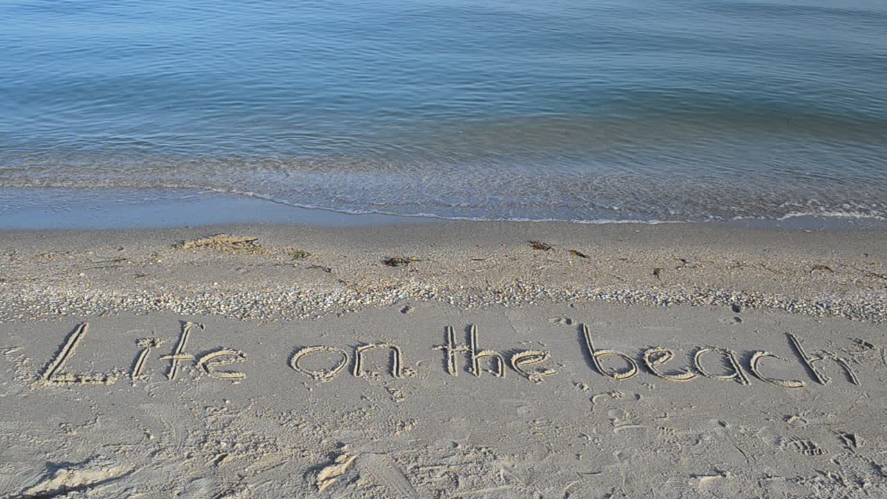 Concetto di vita da spiaggia - iscrizione sulla sabbia con un'onda in arrivo. Iscrizione sulla sabbia.