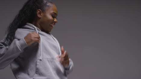 Studio-Portrait-Shot-Of-Young-Woman-Wearing-Hoodie-Dancing-With-Low-Key-Lighting-Against-Grey-Background-16