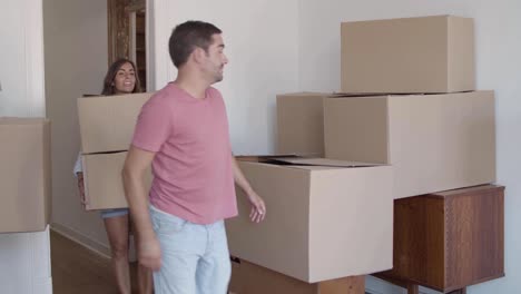 young boyfriend and girlfriend entering room and carrying cardboard boxes