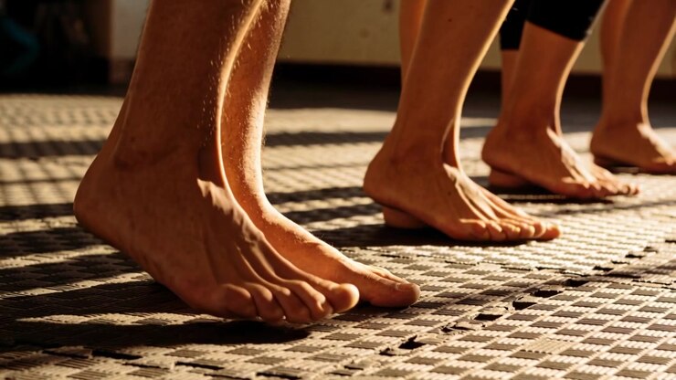 Seguendo l'indicazione dell'istruttore, una fila di piedi esegue sollevamenti dei talloni per l'allenamento su un tappetino di gomma, con pantaloncini.