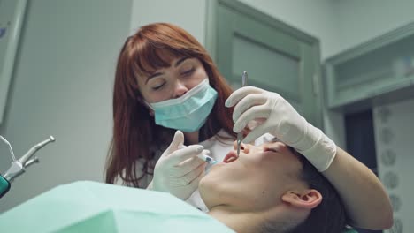female stomatologist applying anesthetic injection before oral surgery operation in clinic. pretty dentist using mouth mirror and medicine syringe during her work. close-up