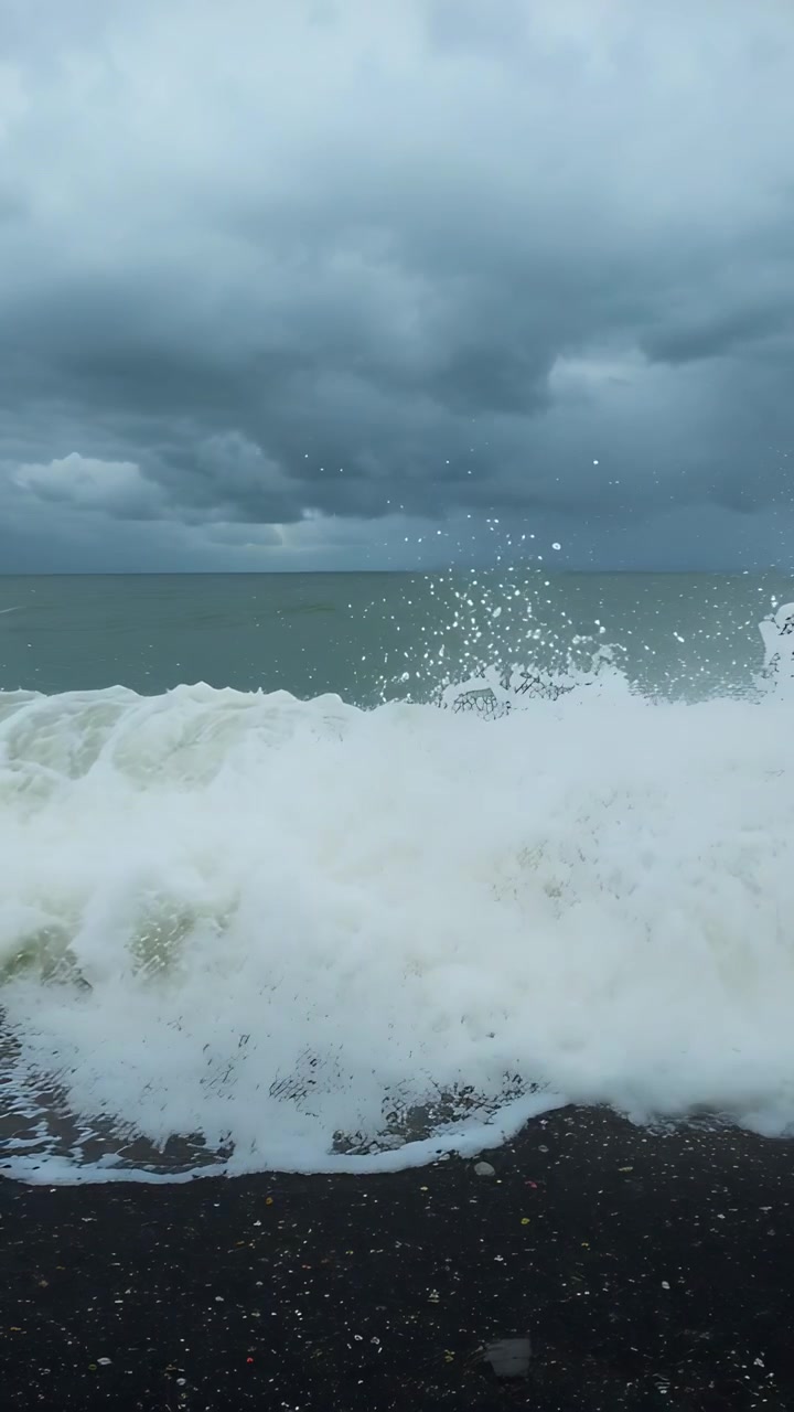 Vertical video: Surging breaking sea wave crashing onto pebble shore from storm swell, making foam