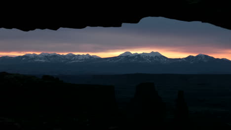 clouds of darkness lighten into delicate shades of pink as the sun rises over mesa arch in canyonlands national park