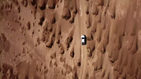 Cenital-shot-of-a-white-car-driving-in-the-desert,-top-down-view-of-a-vehicle-driving-off-road