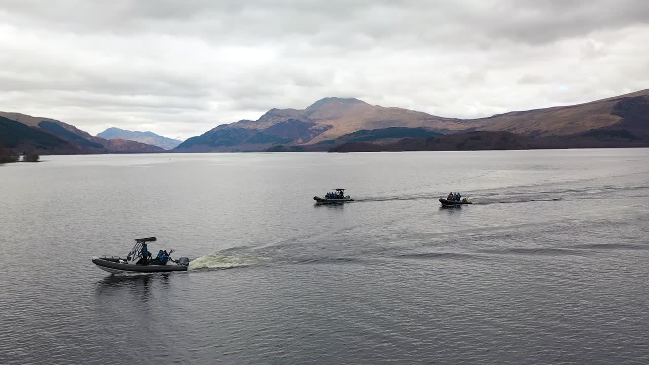 toma aérea cinematográfica de drones barriendo alrededor de 3 barcos navegando en loch lomond escocia con ben lomond en el fondo a principios de la primavera