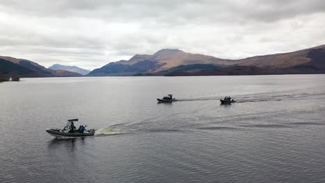 cinematic aerial drone shot sweeping around 3 boats cruising on loch lomond scotland with ben lomond in the background in early spring