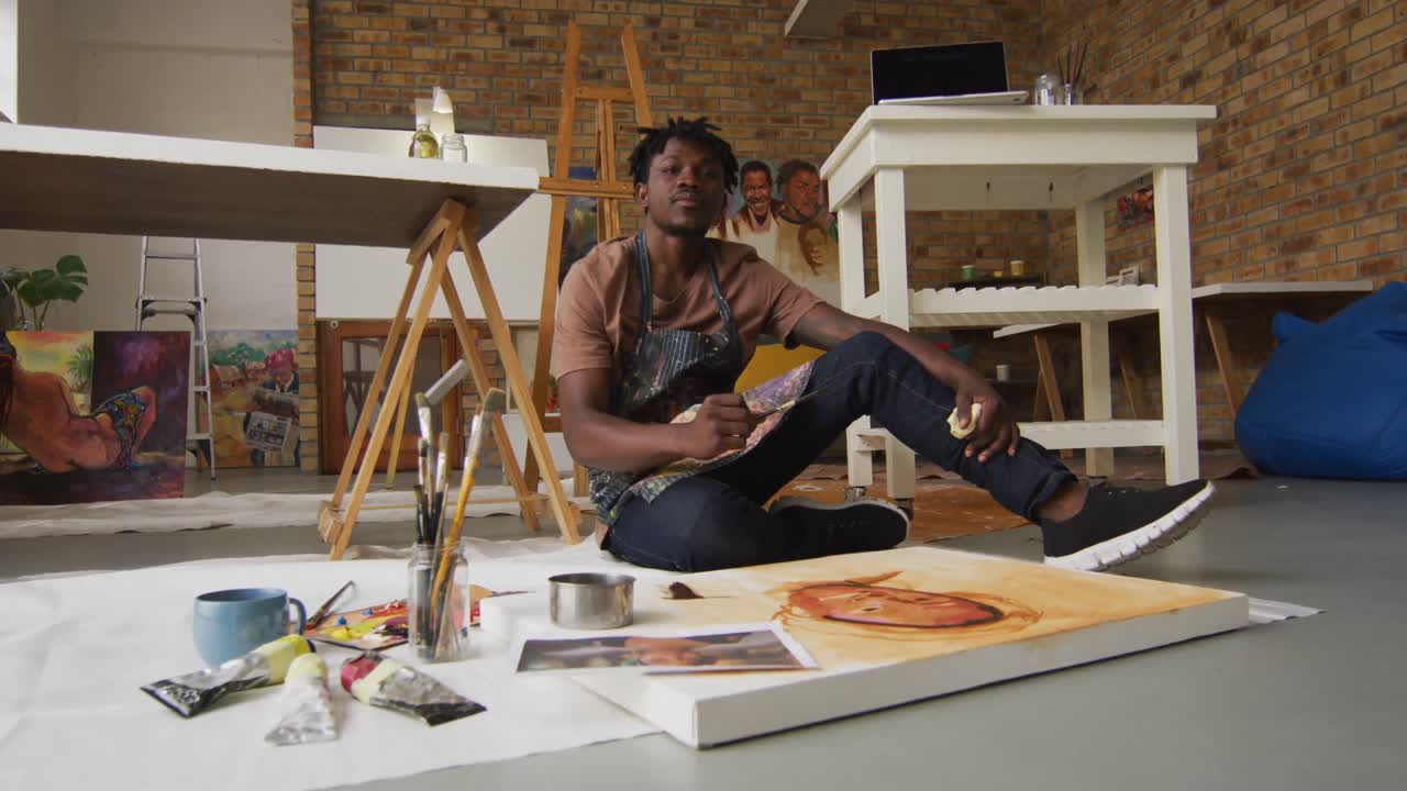 Portrait of smiling african american male artist wearing apron painting on canvas at art studio