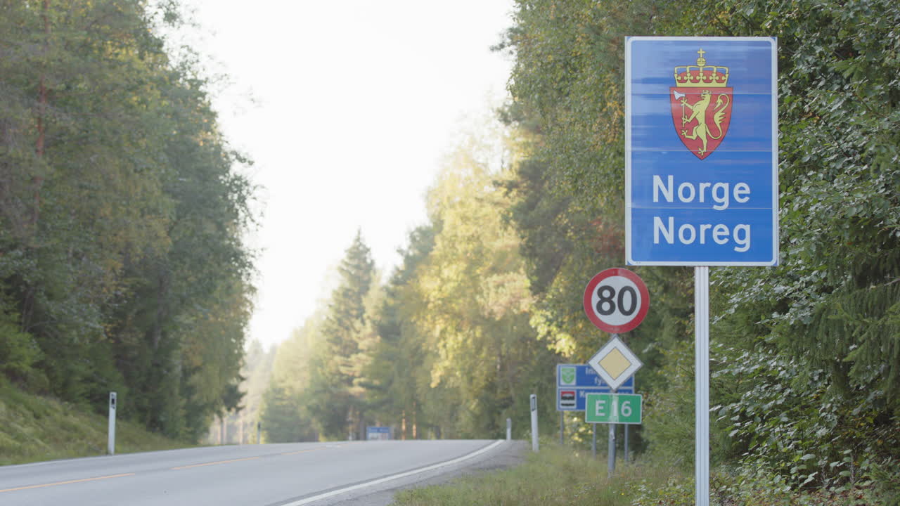 Car drives past blue roadside Norwegian road sign on border with Sweden