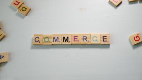 a table with scattered wooden letters and a person spelling commerce