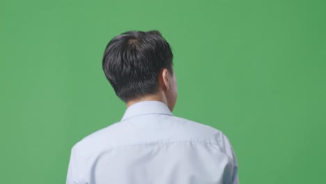 back view close up of asian business man walking and looking around on green screen background in the studio