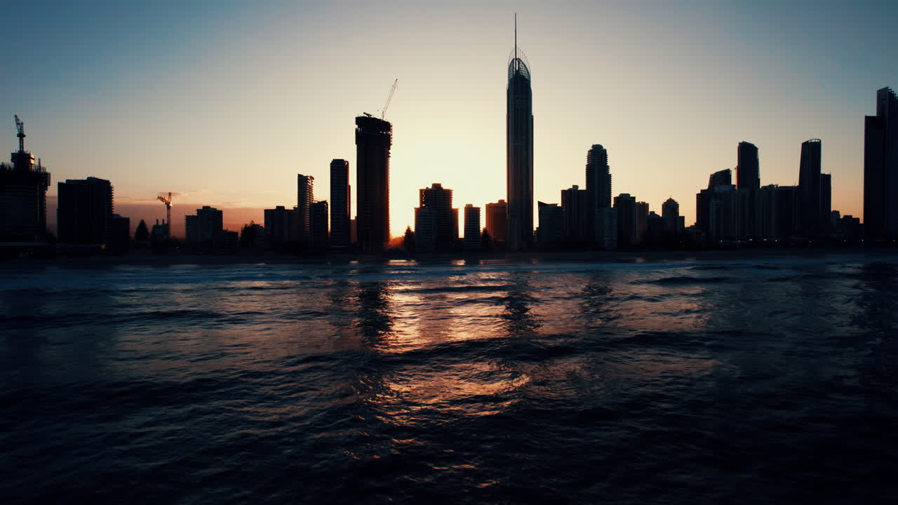 Stunning drone footage of the Gold Coast’s Surfers Paradise skyline during golden hour, showcasing the city’s beachfront high-rises with the ocean glowing in the evening light