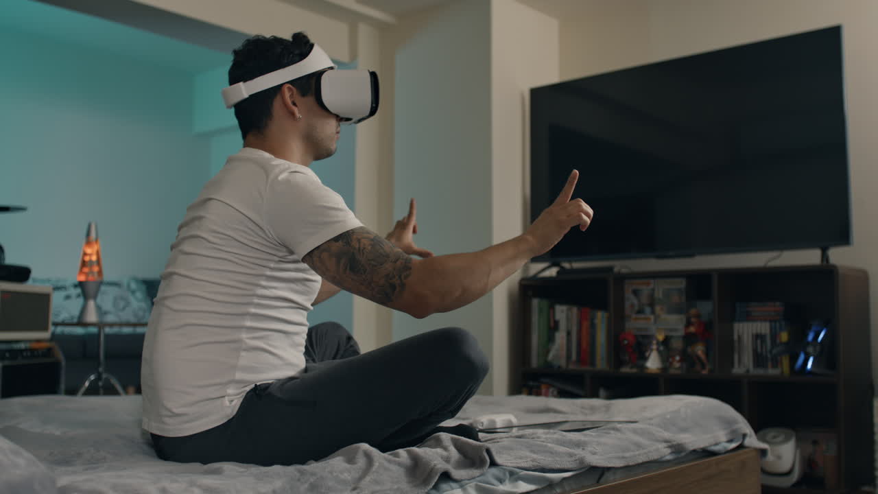 Man puts on virtual reality headset while sitting on bed in modern home setup