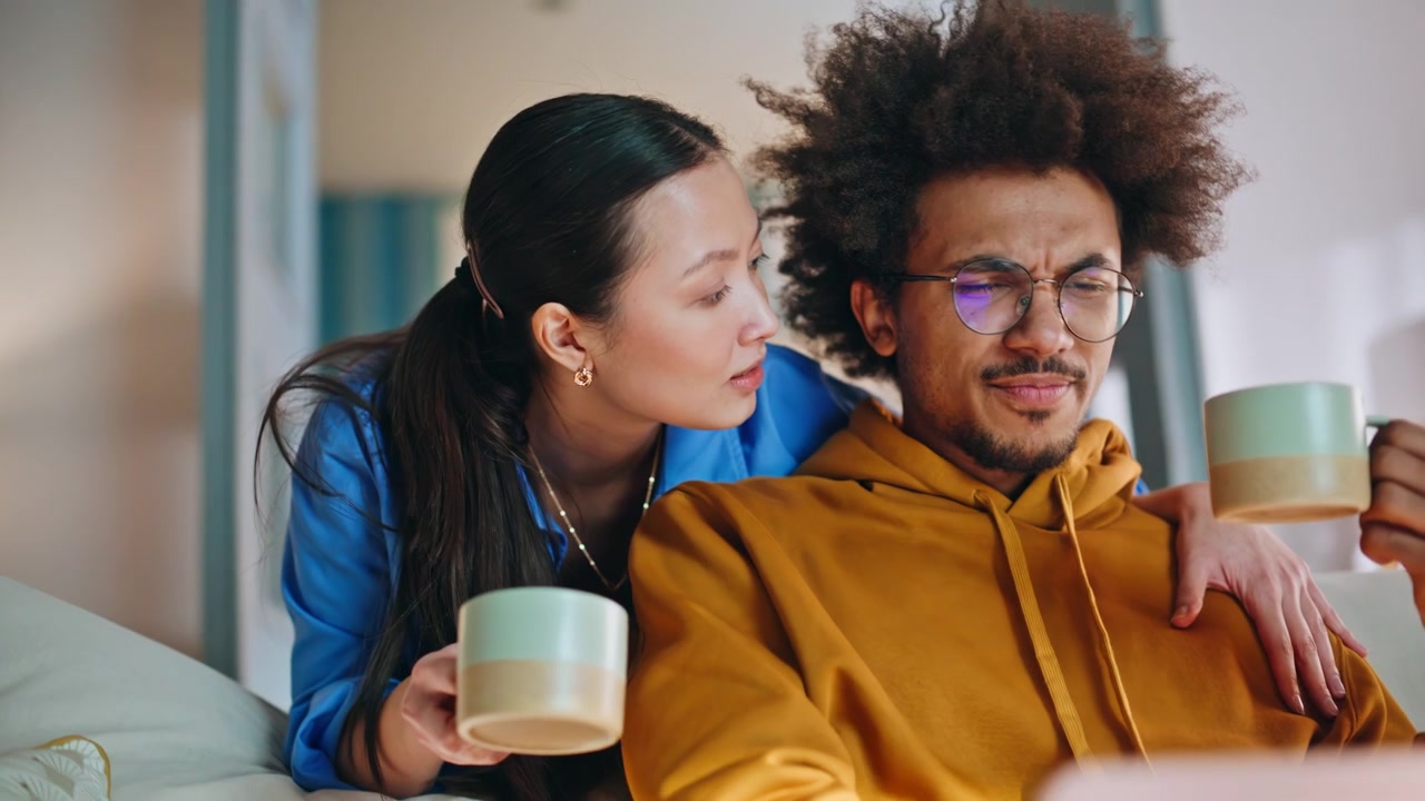 Couple watching laptop home sofa closeup. Woman hugs boyfriend drinking coffee.