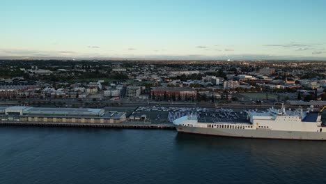 Vuelo-Aéreo-Hacia-Adelante-Sobre-El-Puerto-De-Fremantle-Con-Muelle-Con-Un-Gran-Barco-Y-La-Ciudad-De-Perth-En-Segundo-Plano