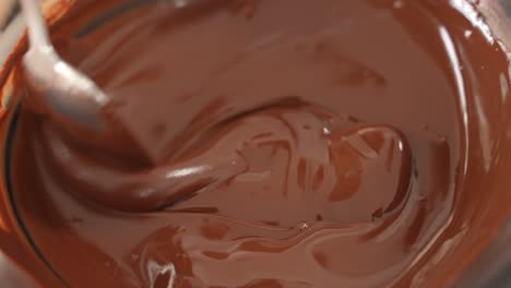 mixing melted chocolate in steel bowl with spoon, slow motion close up