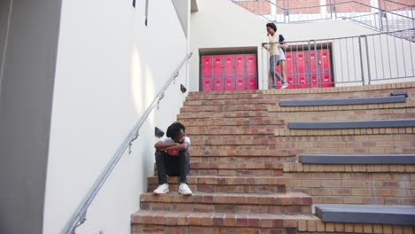 sitting on stairs, boy feeling sad while two girls watching in school, copy space