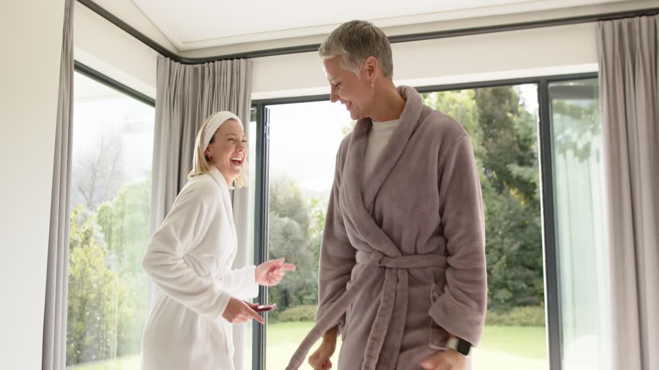 Mother and daughter tapping smartphone to select music and dancing at home near sliding glass doors