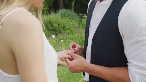 Happy-diverse-couple-with-ring-holding-hands-on-sunny-day-at-wedding