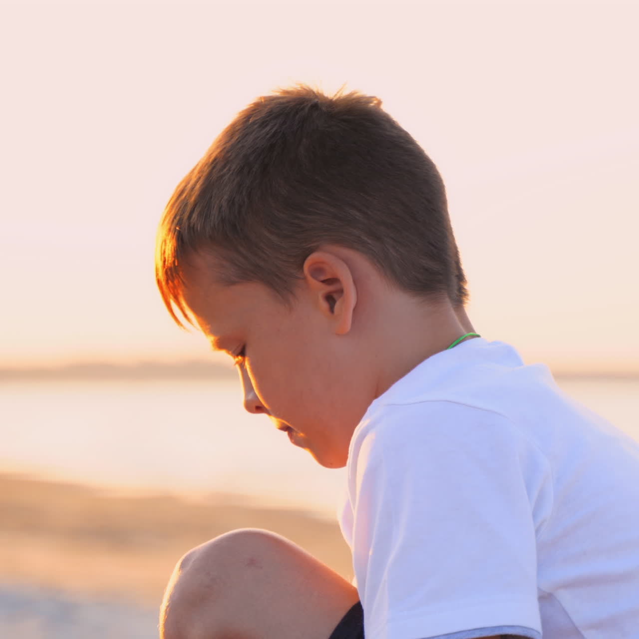 Side view of a boy in the sea shore. Boy is sitting on the sand beach in the evening at sunset. Close-up. Summer vacation.