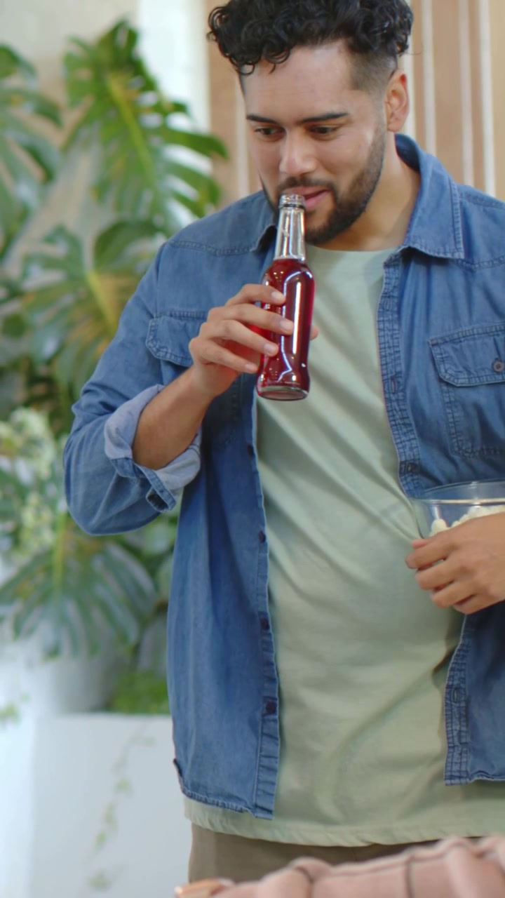 Video verticale: Uomo sorridente sposta una bottiglia, sorseggia una bevanda mentre interagisce con un amico in un lounge, popcorn.