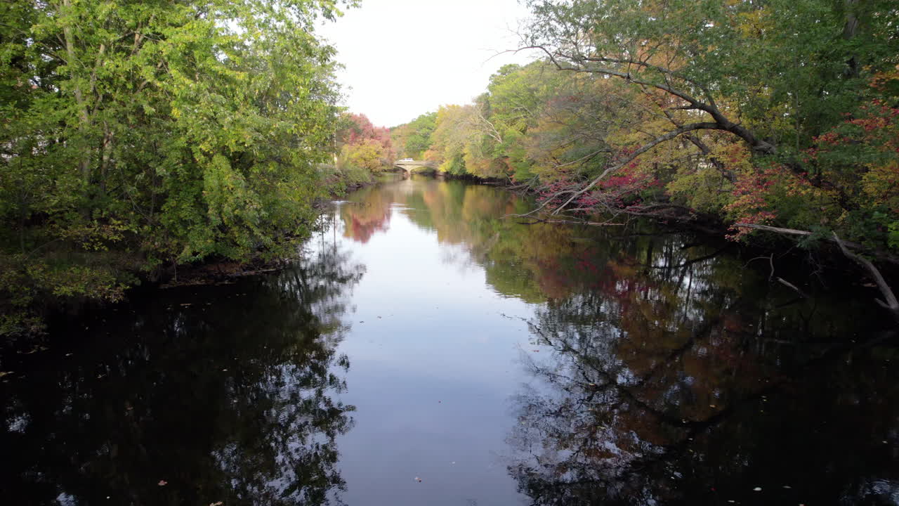 Slow aerial drone view of the peaceful Pawtuxet River in Cranston, Rhode Island. Beautiful fall foliage lines the calm waters in this slow aerial video