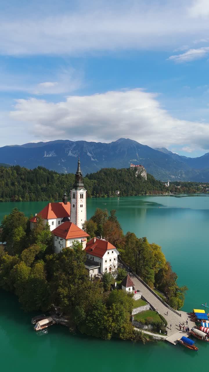 Verticale, aerea: vista dell'isola del lago di Bled con il castello di Bled in lontananza durante il giorno a Bled, Slovenia, ripresa con drone in avvicinamento