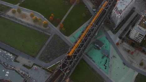 Iconic-Typical-Berlin-Subway-Train-in-yellow-color-passing-a-bridge-through-Public-Park-in-Germany,-Aerial-Birds-Eye-Overhead-Top-Down-View