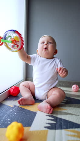 happy smiling kid sits on the floor holding a toy. lovely child plays at home. vertical video.