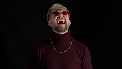 elegante joven sonriente con gafas de sol rojas mirando a la cámara, riendo en voz alta, sintiendo felicidad