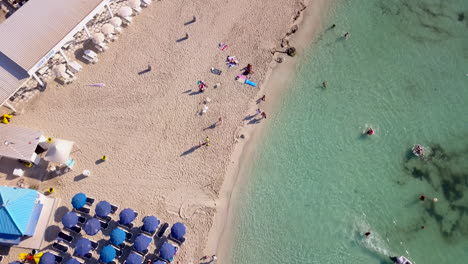 Aerial-shot-of-a-sandy-beach-with-people-and-beach-facilities-at-a-holiday-resort