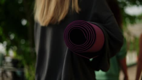 Rear-view-women-go-together-for-exercise-holding-mats-for-yoga,-Close-Up