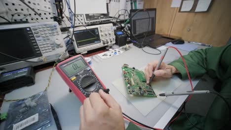 electronic equipment repair shop. the engineer technician solders the printed circuit board of an electronic device under a microscope.